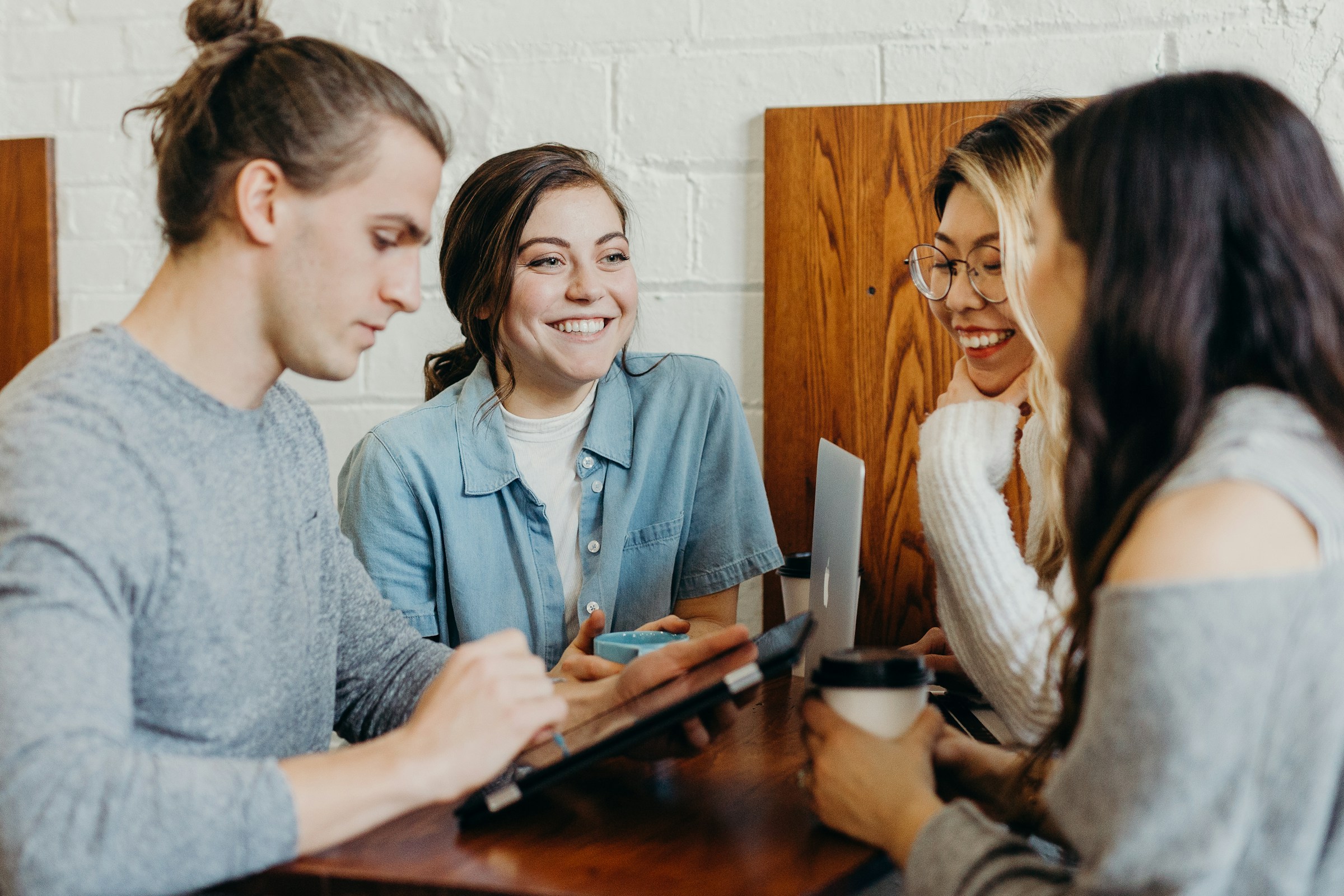 Four college students working together around a table with a laptop and tablet